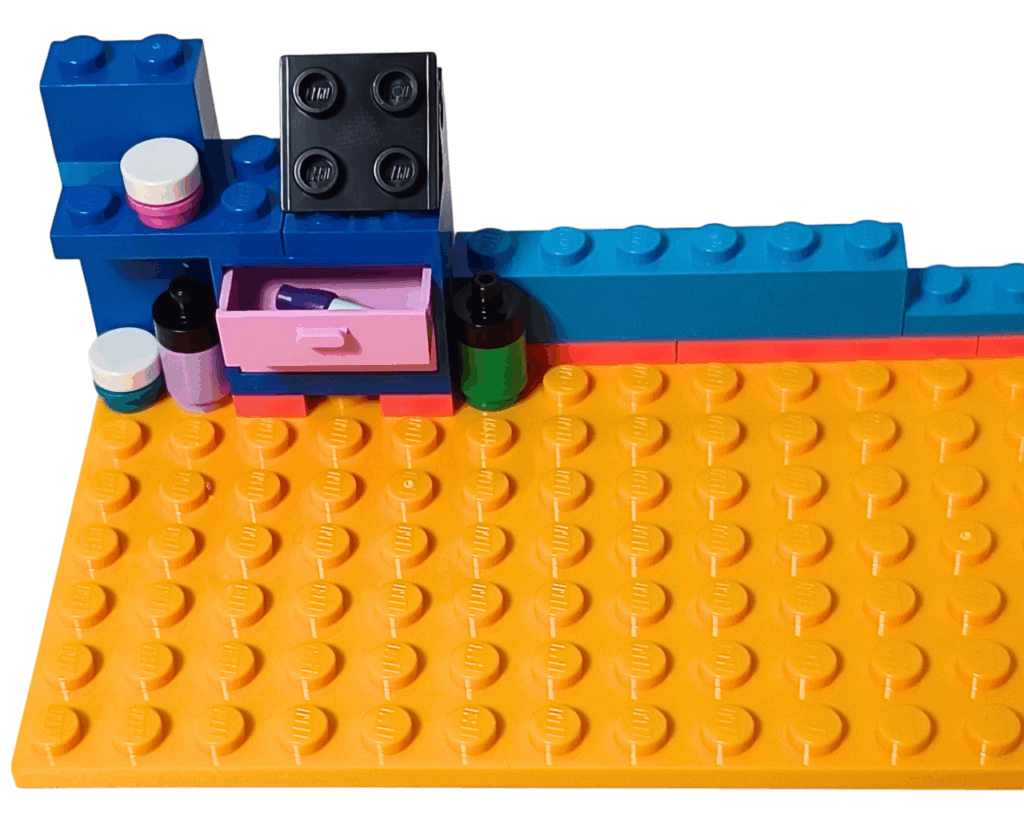 LEGO Friends 41739 リアンの部屋 壁と棚の組立。 オレンジの基盤の左奥に、ブルーの壁と棚が組まれ、ピンクの引き出しの中にはペンが入っている。棚の上には緑・紫・黒などの丸いインクボトルパーツが並ぶ。