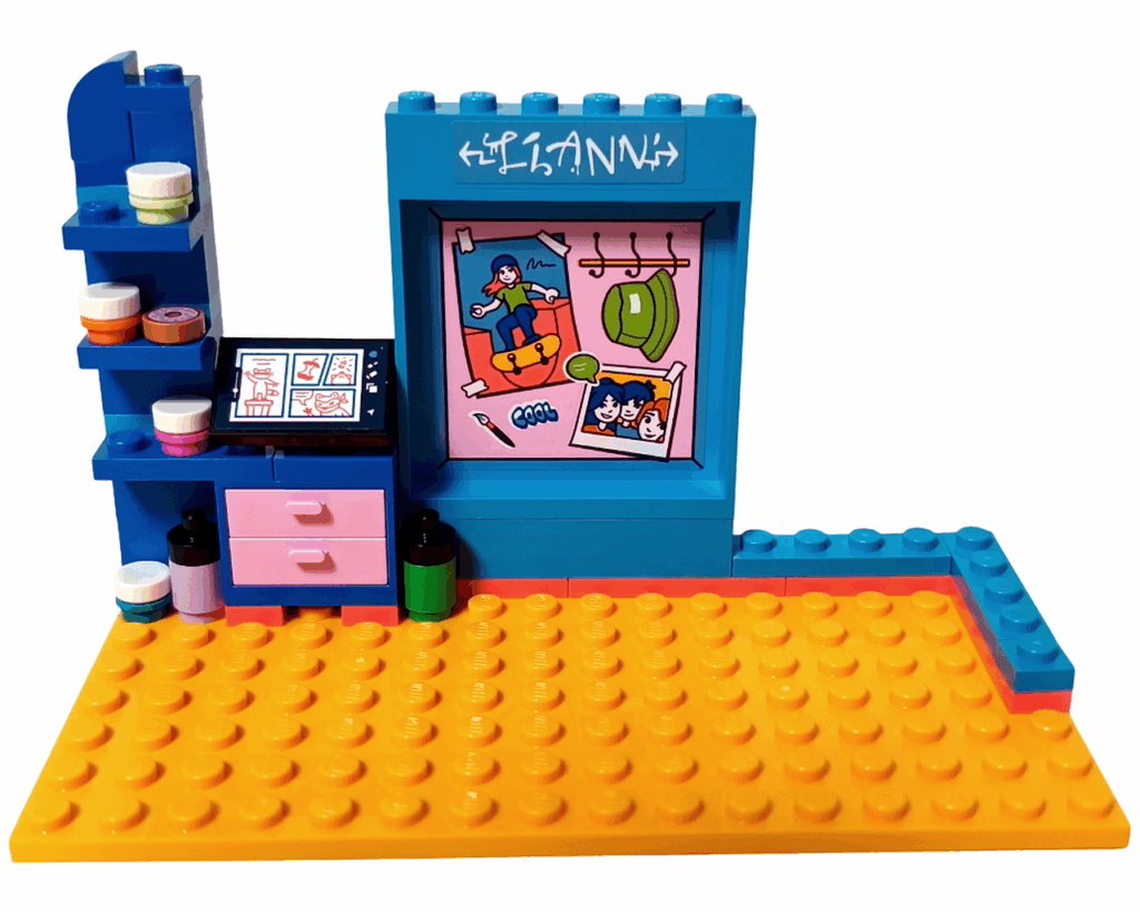 LEGO Friends 41739 リアンの部屋 イラストデスク完成。 左側に青い棚とピンクの引き出し、上には丸いインクボトルが並ぶ。 中央の壁には「LIANN」の文字と、スケートボードに乗る人物や友人たちの絵が描かれたステッカーが貼られている。 机の上にはイラストが描かれた黒いタブレットパーツが配置されている。