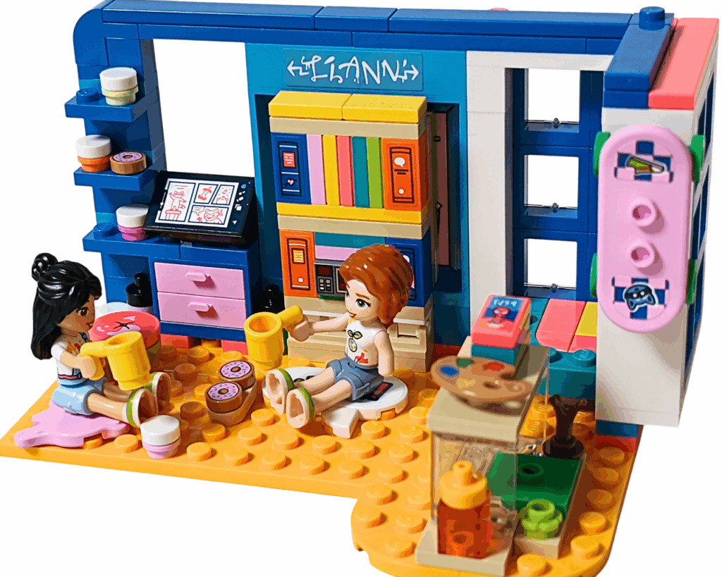 LEGO Friends 41739 リアンの部屋 完成シーン。 リアンとオータムがカップを持って座り、床にはドーナツとピンクのラグがある。 背後の棚にはタブレットや絵の具、壁にはスケートボードが飾られている。
