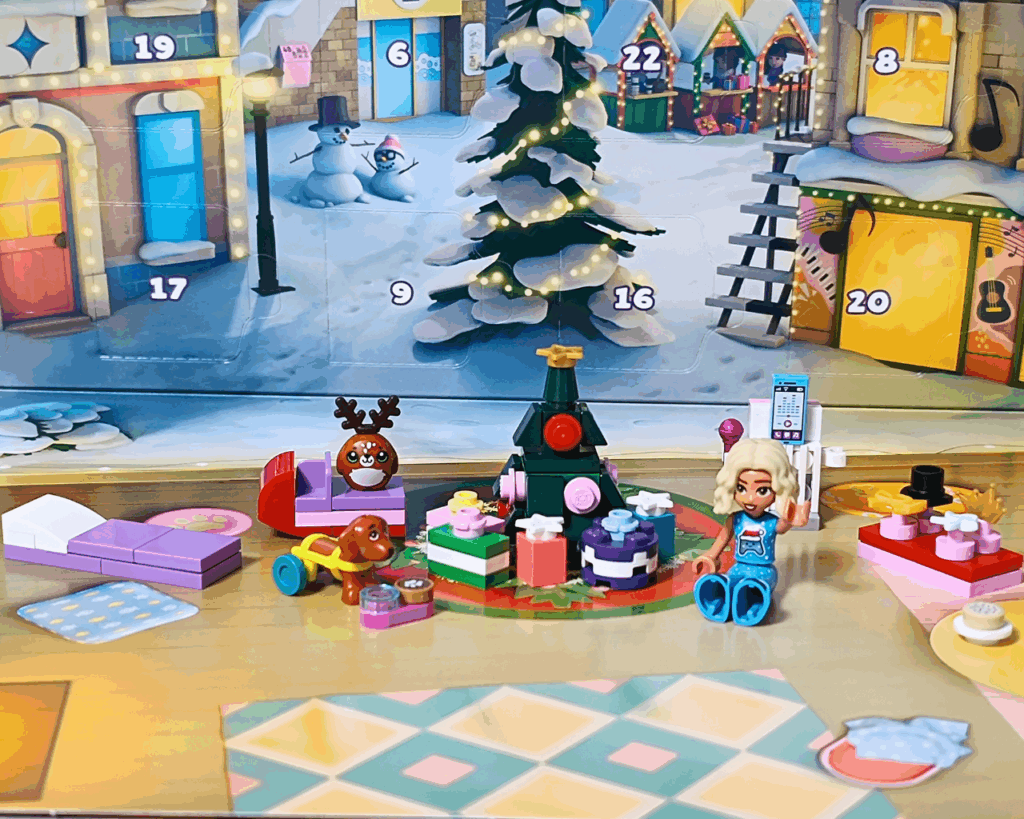 LEGO Friends 42668 第3部まとめシーン。中央にノヴァが座り、 まわりにクリスマスツリー、プレゼント、ピクルス、トナカイ人形、ベッド、 カラオケセットなどが並ぶ。背景にはアドベントカレンダーの街並みが見える。