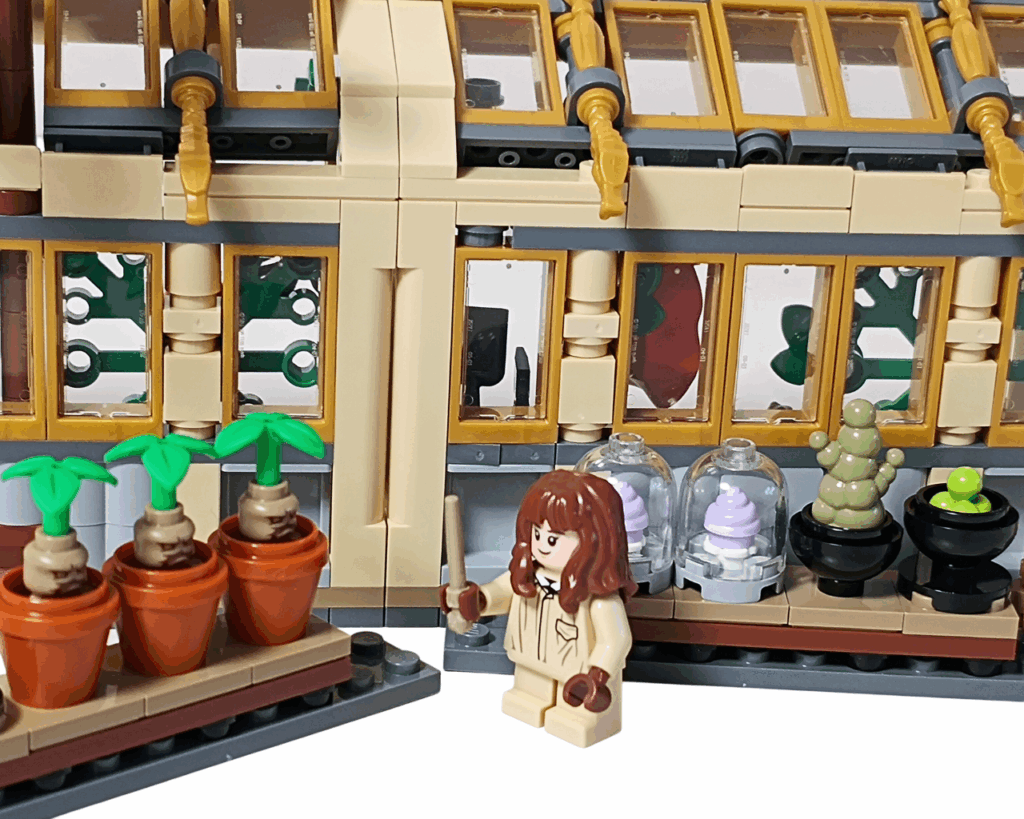 LEGO Harry Potter 76445 ホグワーツ城：薬草学の授業 ハーマイオニーの観察シーン。 ハーマイオニーが杖を持って魔法植物標本を見つめ、背後に3つの鉢植えと透明ドーム入り標本が並ぶ。 窓越しに温室の外の光が差し込んでいる