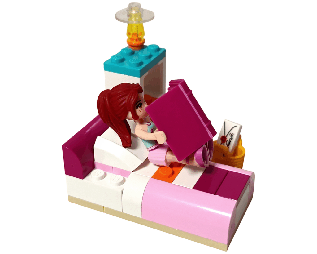 ベッドに寝転んで日記を読むミア。後ろには棚やランプがあり、ドラム演奏を終えた後のリラックスした雰囲気