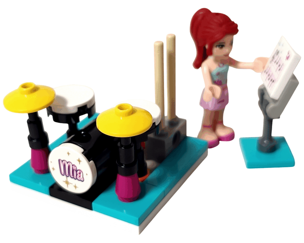 ミニドールのミアが譜面台に手を伸ばし、横には黄色いシンバル付きのドラムセットがある