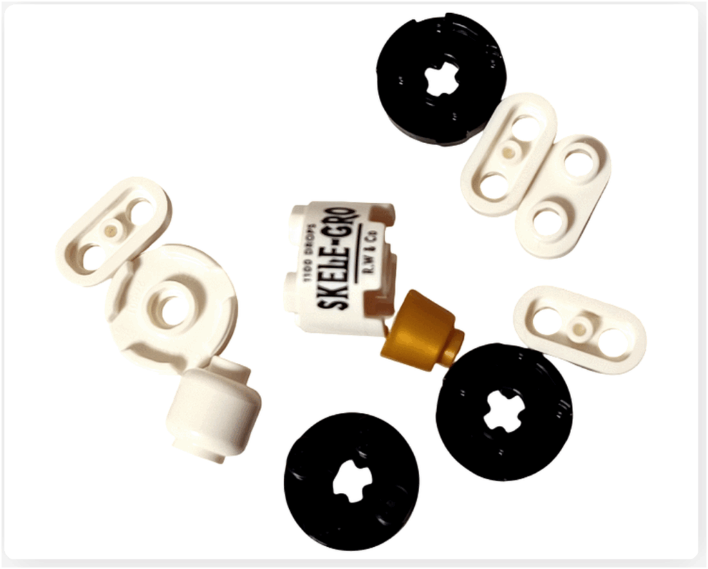 LEGO Harry Potter 76456 アドベントカレンダー2025 18日目のパーツ。 白と黒の円形パーツや、「SKELE-GRO」と印字された白いボトル型プリントパーツ、金色のフタパーツなどが含まれる。