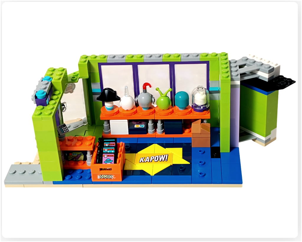 レゴ フレンズ 42674 組立レビューの写真。SFテーマのコミック4冊がオレンジ色のコミックストックボックスに収納され、店内床のKAPOW!タイル前に配置されている。