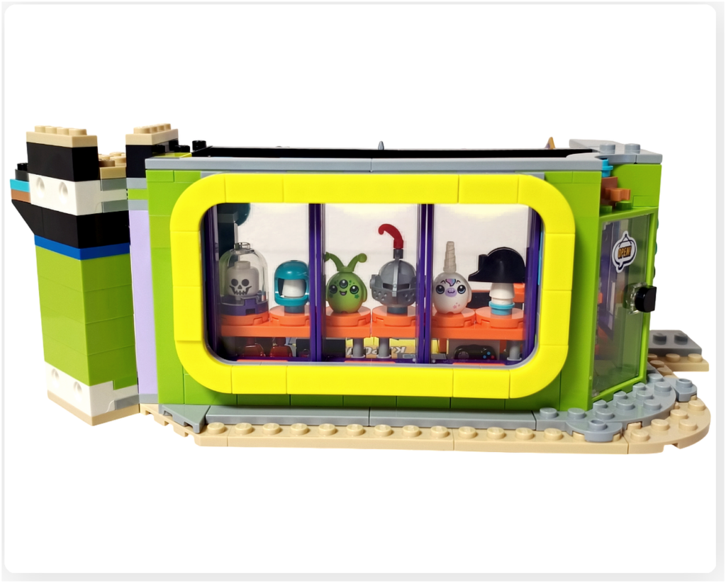 レゴ フレンズ 42674 組立レビューの写真。コミックショップとゲームセンターの外観で、黄色いフレームの大きなディスプレイウインドウ内に、ファンタジー風やSF風のヘルメットやキャラクターアイテムが並べられている。