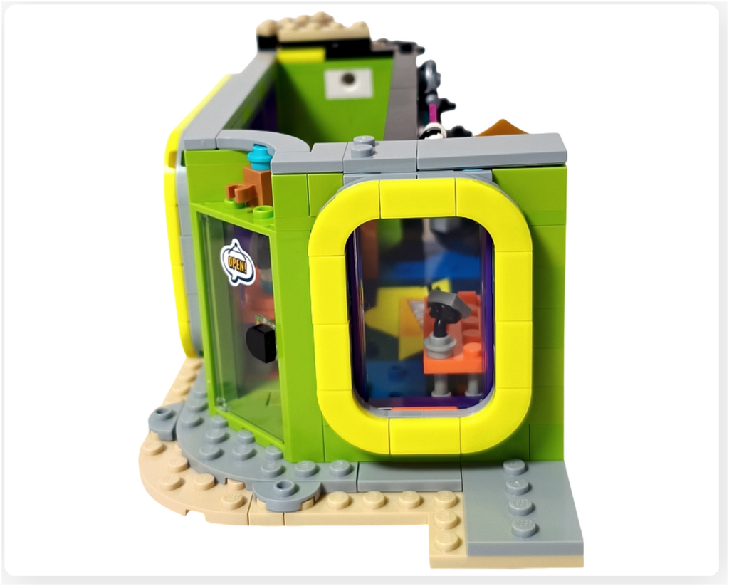 レゴ フレンズ 42674 組立レビューの写真。コミックショップとゲームセンターの外観で、レジ側に配置されたサイドウインドウ越しに、店内のレジカウンターと小物ディスプレイが見える様子。