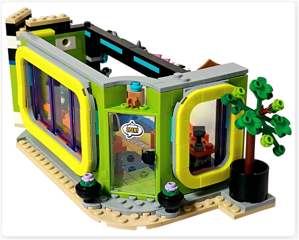レゴ フレンズ 42674 組立レビューの写真。コミックショップとゲームセンターの入口周辺に植木が配置され、ガラス扉とウインドウを囲む外観が完成している様子。
