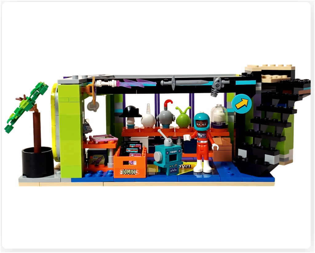 レゴ フレンズ 42674 コミックショップとゲームセンターの1階完成写真。ヘルメットのディスプレイ棚、コミックストックボックス、レジ、ロボットフィギュアとミニドールが配置された店内の様子。