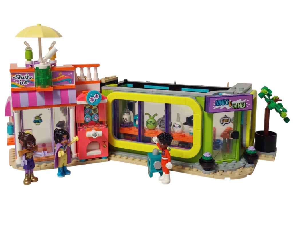 レゴ フレンズ 42674 組立レビュー第2部のエピローグ写真。フローズンドリンクのお店とコミックショップ&ゲームセンターが連結され、ミニドールたちが立つ街角の完成風景。ショップの看板やディスプレイが並ぶ外観全体を写した状態。