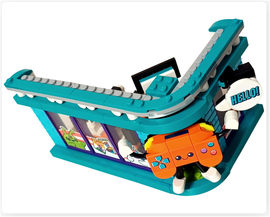 レゴ フレンズ 42674 コミックショップとゲームセンターの外装デザイン。曲線の屋根構造とコーナー部分に取り付けられたゲームコントローラー型マスコット、「HELLO!」の吹き出し看板が特徴的な外観装飾の様子。