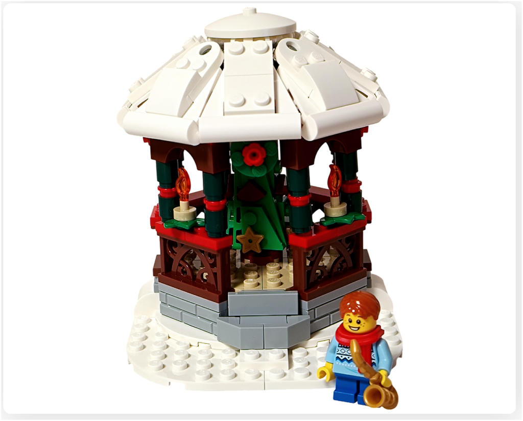 レゴ 40778 雪のあずまや（Winter Gazebo）の完成シーン。白い屋根のあずまやの前に、赤いマフラーと青い服を着たサックス奏者のミニフィグ1体を配置し、冬の広場で最初に音を奏でる情景を表現している。